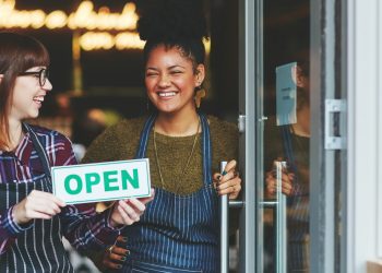 Shot of two young women holding up an open sign in their coffee shop